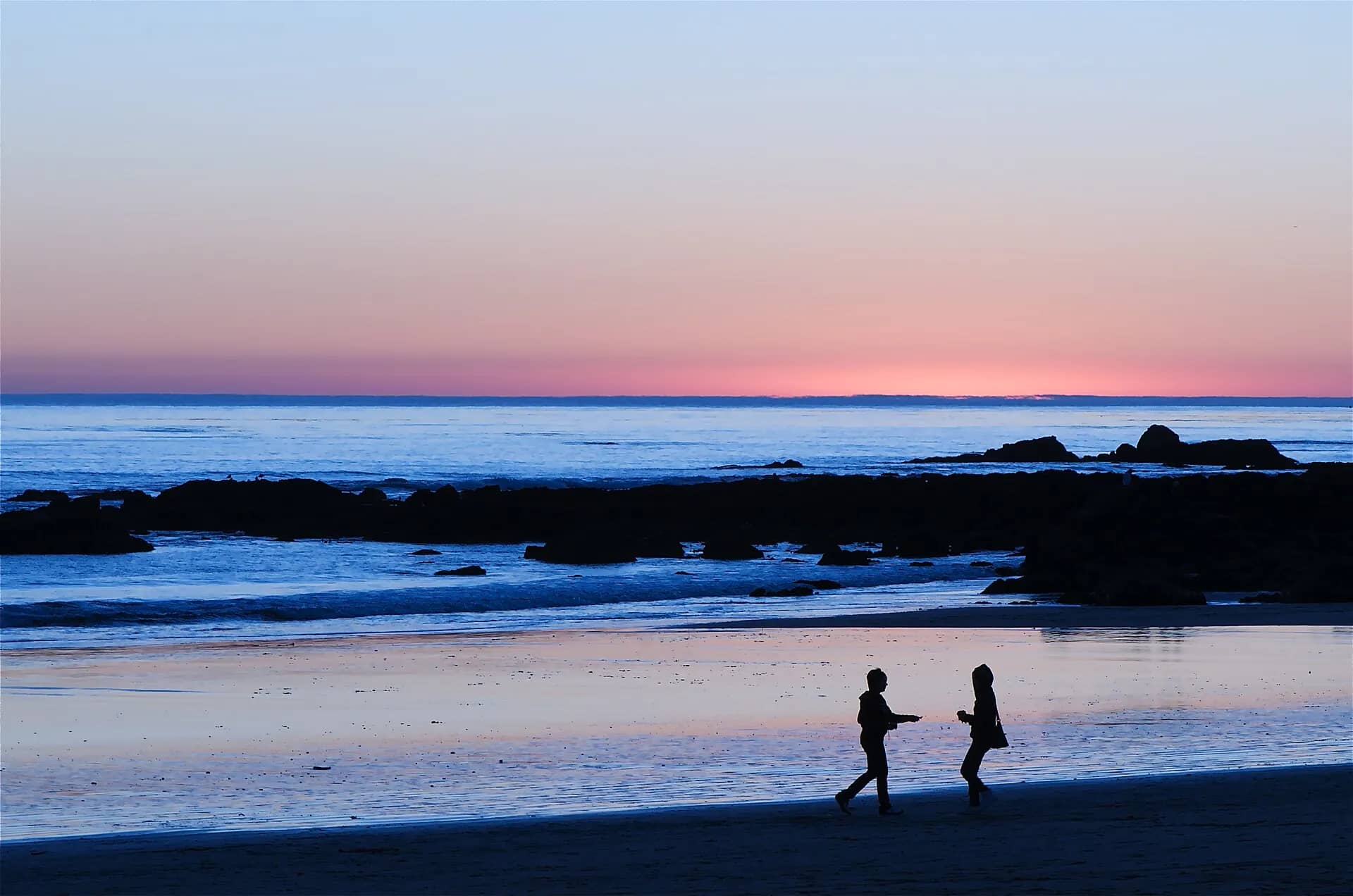 Two people dancing along the shoreline at dusk