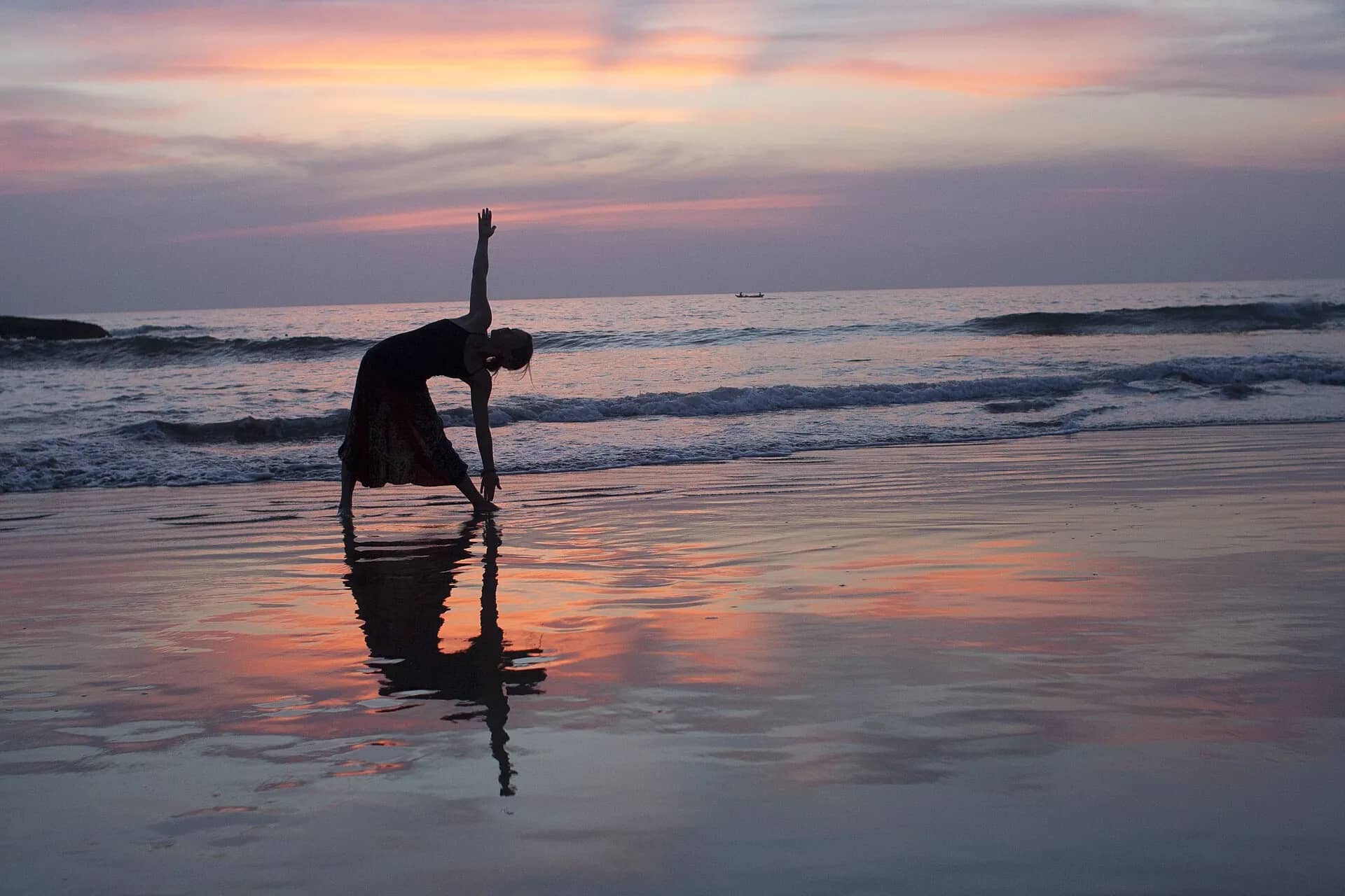 A dancer holding a pose, mirrored in the wet sand at sunset