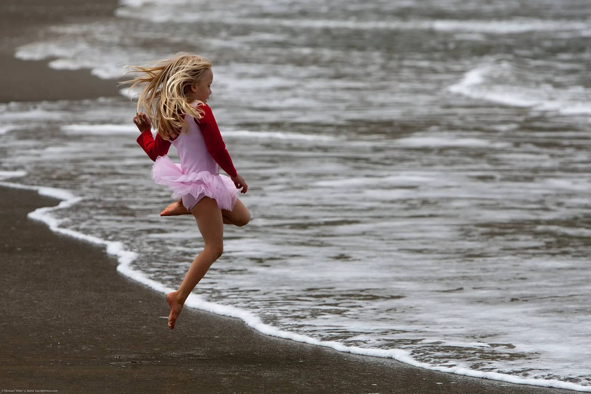A young girl leaping joyfully at the water’s edge