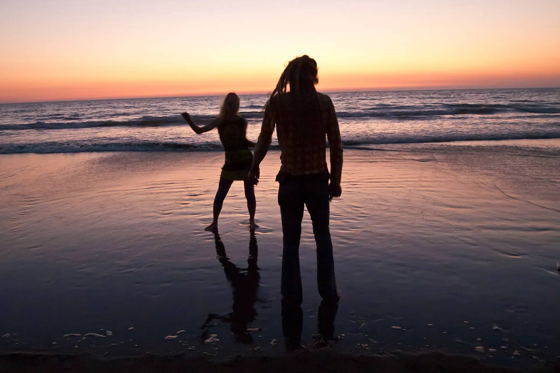Two friends dancing at the water’s edge on Morjim beach at dusk